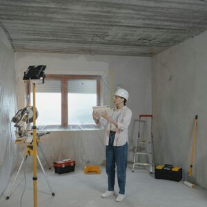 Woman with hard hat and tablet assessing a residential renovation site.